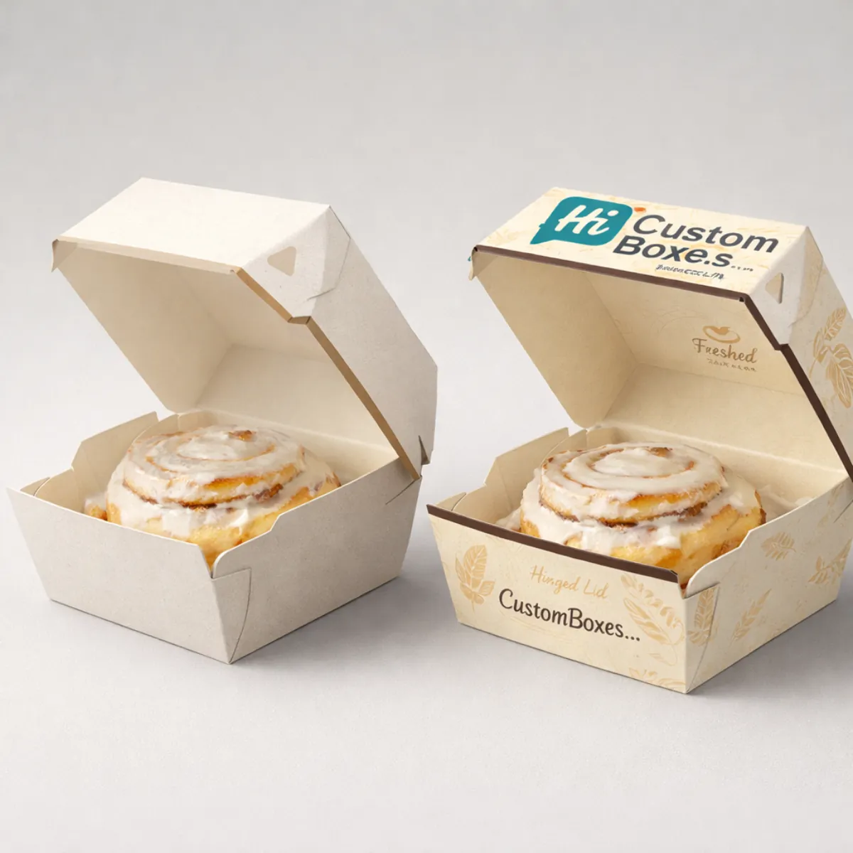 Two individual-serving hinged cardboard boxes, each containing a large, freshly glazed cinnamon roll with decorative branding. class=